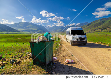 Green trash bin overflowing with garbage on rural dirt road Green trash bin overflowing with garbage on rural dirt road 135450595