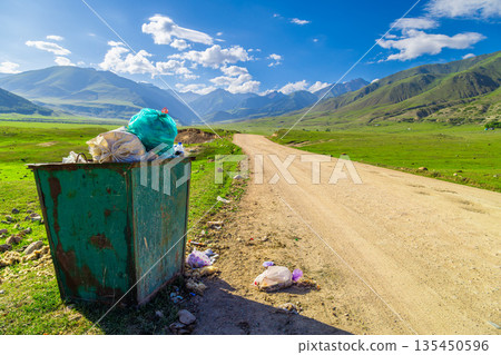 Overflowing trash can amidst rural mountainous landscape Overflowing trash can amidst rural mountainous landscape 135450596