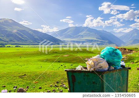 Green metal trash container overflowing with trash in mountain valley Green metal trash container overflowing with trash in mountain valley 135450605