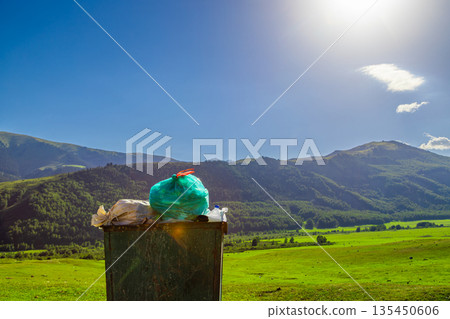 Weathered trash bin filled with garbage in green meadow Weathered trash bin filled with garbage in green meadow 135450606
