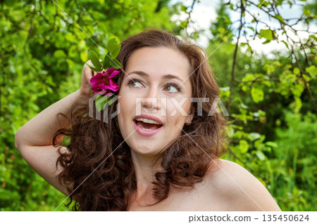 Beautiful young brunette girl with perfect skin holding red rose flower in hand on park or garden green background. Beauty nature skincare eco organic cosmetic ecology pure health concept Beautiful young brunette girl with perfect skin holding red rose flower in hand on park or garden green background. Beauty nature skincare eco organic cosmetic ecology pure health concept 135450624