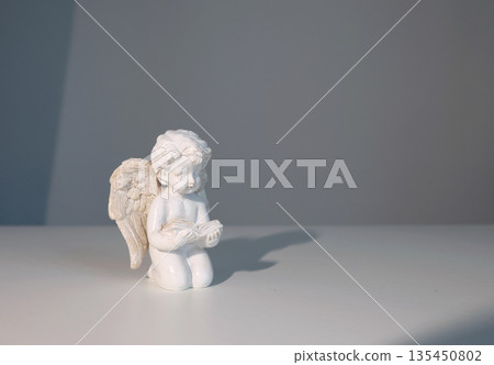 White ceramic angel figurine on white background for design. Faith, symbols, and traditions. 135450802