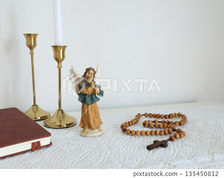 Catholic corner at home. Angel figurine, wooden rosary beads, cross, and prayer book. Faith, symbols, and traditions. Catholic corner at home. Angel figurine, wooden rosary beads, cross, and prayer book. Faith, symbols, and traditions. 135450812