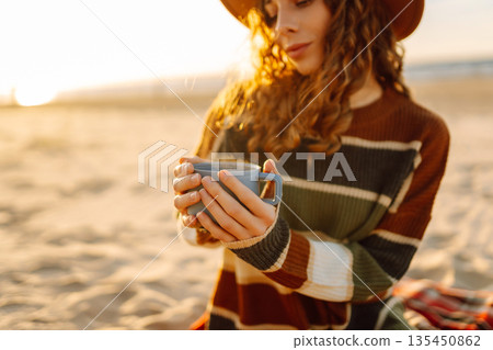 Young happy traveler tourist sits at picnic on the beach drinks hot drink. People, journey concept 135450862