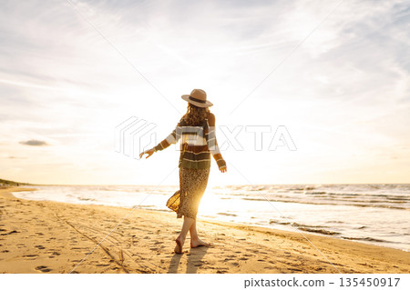 Beautiful woman at the windy spring day relaxing on coast. Carefree lady looking at the sunset. 135450917