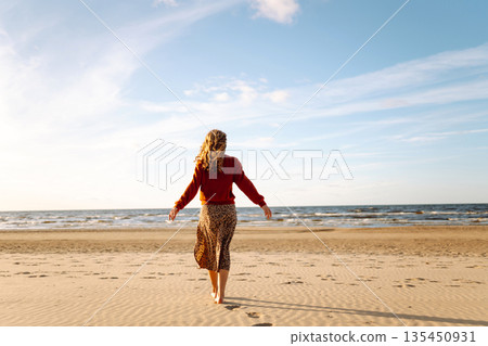 Beautiful woman on the beach in cold weather enjoying time in the sunset. Lifestyle, adventure. Beautiful woman on the beach in cold weather enjoying time in the sunset. Lifestyle, adventure. 135450931