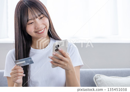 年輕女子手持智慧型手機和信用卡 135451038