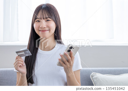 年輕女子手持智慧型手機和信用卡 135451042