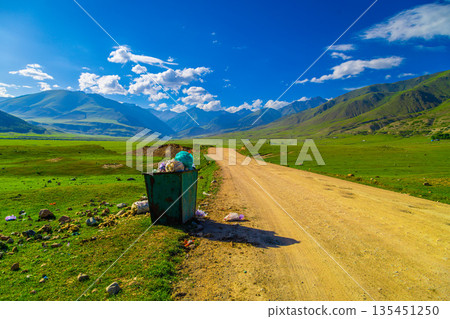 Overflowing green trash bin on dirt road in rural landscape Overflowing green trash bin on dirt road in rural landscape 135451250