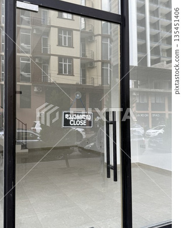Closed storefront door with bilingual close sign in urban environment reflection background Closed storefront door with bilingual close sign in urban environment reflection background 135451406