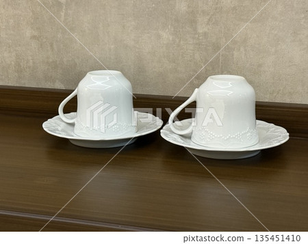 Upside down white teacups on saucers against a wooden surface background 135451410