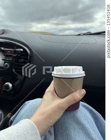 Person holding coffee cup inside a car with sky view from window Person holding coffee cup inside a car with sky view from window 135451416