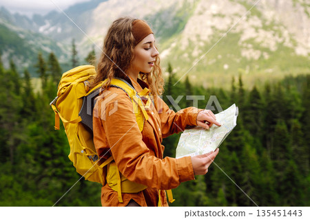 The adventure begins! Beautiful woman traveler with a yellow backpack, holds a map. Vacation concept 135451443