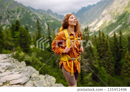 Young traveler woman with a yellow backpack on a cliff. Sports concept, traveler. Active lifestyle. Young traveler woman with a yellow backpack on a cliff. Sports concept, traveler. Active lifestyle. 135451496