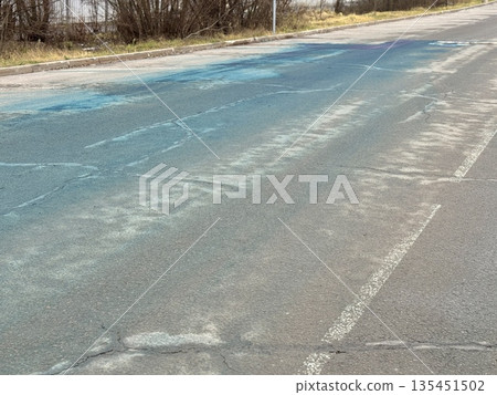 A Blue Chemical Stain On The Asphalt Of The Road, On Which Uneven Spots Of Bright Blue Liquid Are Visible, Accumulated In Puddles And Smeared On Faded Markings And Cracked Asphalt. A Blue Chemical Stain On The Asphalt Of The Road, On Which Uneven Spots Of Bright Blue Liquid Are Visible, Accumulated In Puddles And Smeared On Faded Markings And Cracked Asphalt. 135451502