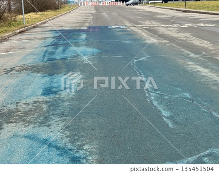 A Blue Chemical Stain On The Asphalt Of The Road, On Which Uneven Spots Of Bright Blue Liquid Are Visible, Accumulated In Puddles And Smeared On Faded Markings And Cracked Asphalt. 135451504