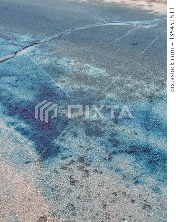 A Blue Chemical Stain On The Asphalt Of The Road, On Which Uneven Spots Of Bright Blue Liquid Are Visible, Accumulated In Puddles And Smeared On Faded Markings And Cracked Asphalt. 135451511