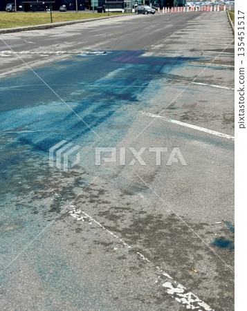 A Blue Chemical Stain On The Asphalt Of The Road, On Which Uneven Spots Of Bright Blue Liquid Are Visible, Accumulated In Puddles And Smeared On Faded Markings And Cracked Asphalt. A Blue Chemical Stain On The Asphalt Of The Road, On Which Uneven Spots Of Bright Blue Liquid Are Visible, Accumulated In Puddles And Smeared On Faded Markings And Cracked Asphalt. 135451517