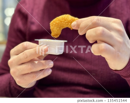 Woman Hand Holding Chicken Nugget Over Sauce, CloseUp Of Casual Eater In Maroon Shirt Dipping Golden Crispy Nugget Into HoneyMustard. Remote Worker Enjoying Quick food. 135451544