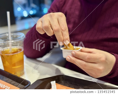 Woman Hand Holding Chicken Nugget Over Sauce, CloseUp Of Casual Eater In Maroon Shirt Dipping Golden Crispy Nugget Into HoneyMustard. Remote Worker Enjoying Quick food. 135451545