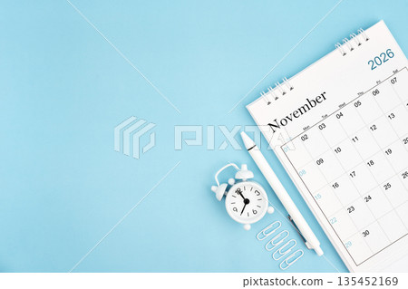 November 2026, Monthly desk calendar for 2026 year and alarm clock with paper clips on blue color background. 135452169