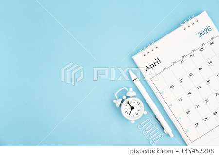 April 2026, Monthly desk calendar for 2026 year and alarm clock with paper clips on blue color background. April 2026, Monthly desk calendar for 2026 year and alarm clock with paper clips on blue color background. 135452208