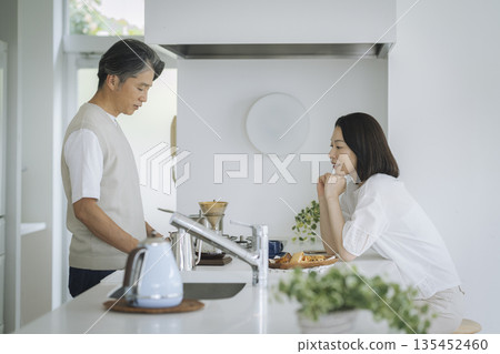 A tired-looking couple in their 50s talking over the kitchen counter 135452460