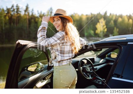 Joyful traveler embraces nature at sunset by lakeside with open car door, freedom, adventure. Joyful traveler embraces nature at sunset by lakeside with open car door, freedom, adventure. 135452586