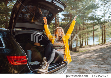 Young woman sits in the trunk of a car in forest. The concept of traveling by car, active lifestyle. 135452673