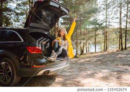 Young woman sits in the trunk of a car in forest. The concept of traveling by car, active lifestyle. 135452674