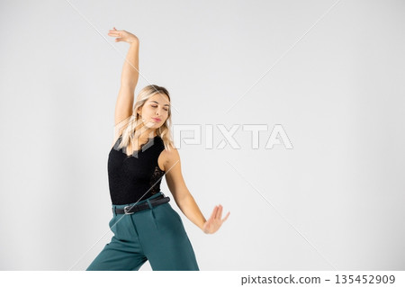 Young blonde dancer posing with hands joined and legs apart on white background 135452909