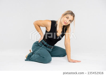 Dancer posing kneeling on white background holding her back 135452916