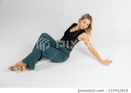 Dancer posing sitting on white floor wearing black top and green trousers 135452919
