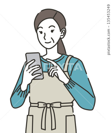 A housewife in an apron looking at her smartphone 135453249
