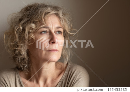 Pensive middle aged woman with curly gray blonde hair looking away, menopause depression anxiety 135453285