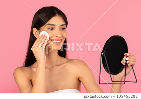 Young beautiful woman removing makeup with cotton pad and holding mirror 135453298