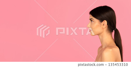 Profile of young woman with ponytail and smooth skin against pink background Profile of young woman with ponytail and smooth skin against pink background 135453310