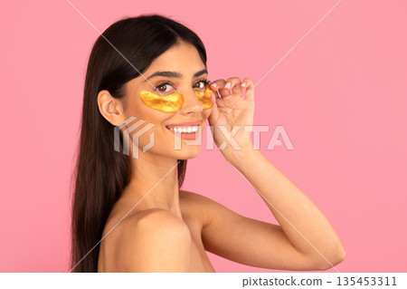 Young woman wearing golden under eye patches and smiling in studio Young woman wearing golden under eye patches and smiling in studio 135453311