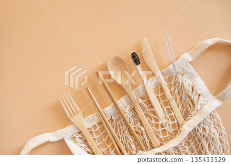 Eco friendly bag and bamboo cutlery set with toothbrush on beige background for green life and zero waste concept. Top view 135453529