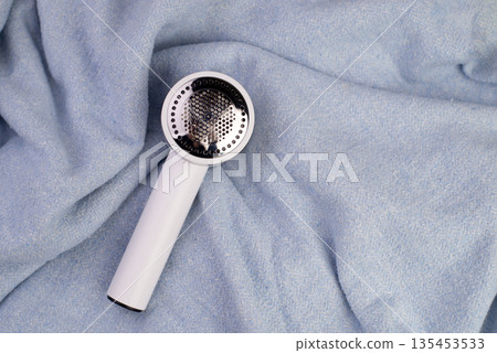 Electric device for removing hair and fluff in blue fabric texture. Shaver for wool. The machine for removing pellets against the background of a knitted sweater. Top view 135453533