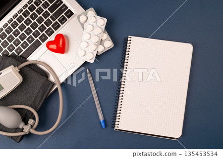 blood pressure meter on laptop with red heart, and pills on dark blue background.paper nootebook with copy space cardiology concept.Tonometer or sphygmomanometer. at the doctor's appointment. top view blood pressure meter on laptop with red heart, and pills on dark blue background.paper nootebook with copy space cardiology concept.Tonometer or sphygmomanometer. at the doctor's appointment. top view 135453534