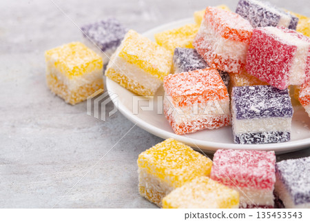 Cubes of multi-colored marmalade in powdered sugar on plate. The concept of baby sweets. Cubes of multi-colored marmalade in powdered sugar on plate. The concept of baby sweets. 135453543