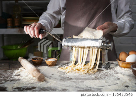 Caucasian female hands making fettuccine noodles using mechanical pasta machine Caucasian female hands making fettuccine noodles using mechanical pasta machine 135453546