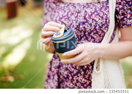 Young female in dress holding reusable silicone foldable coffee tea mug close-up. eco-friendly. mesh cotton bag Young female in dress holding reusable silicone foldable coffee tea mug close-up. eco-friendly. mesh cotton bag 135453551