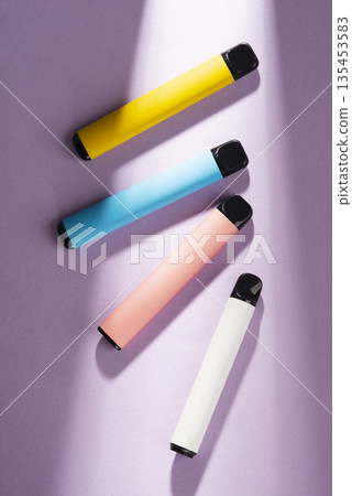 Four colorful disposable electronic cigarettes on a purple background with aesthetic shadows. Minimalist composition of vape pens. Four colorful disposable electronic cigarettes on a purple background with aesthetic shadows. Minimalist composition of vape pens. 135453583