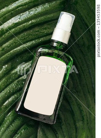 Glass bottle with shampoo or cosmetics product on palm leaves, tropical backdrop. Beauty skin care product template. concept of natural care, eco cosmetics. water drops Glass bottle with shampoo or cosmetics product on palm leaves, tropical backdrop. Beauty skin care product template. concept of natural care, eco cosmetics. water drops 135453598