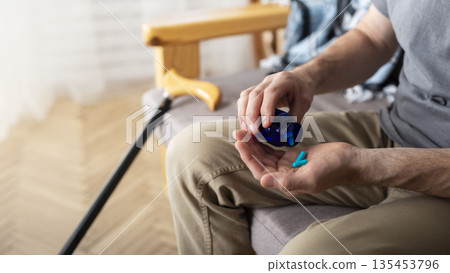 Middle aged caucasian man taking pills sitting on sofa at home Middle aged caucasian man taking pills sitting on sofa at home 135453796