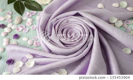 Soft lilac fabric swirled into a rose shape with scattered petals and floral accents 135453904