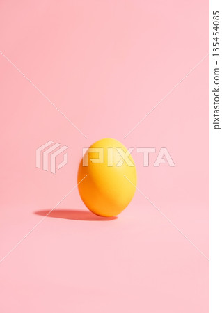 Single yellow Easter egg on pink background, minimal vertical copy space 135454085