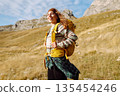 Traveler woman with a bright yellow backpack strolls through golden meadows. Active lifestyle 135454246